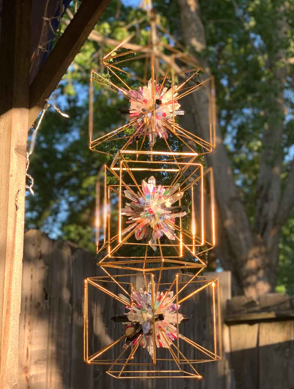 Copper geometric lattice frames holding clusters of crystal, hanging outdoors in daylight