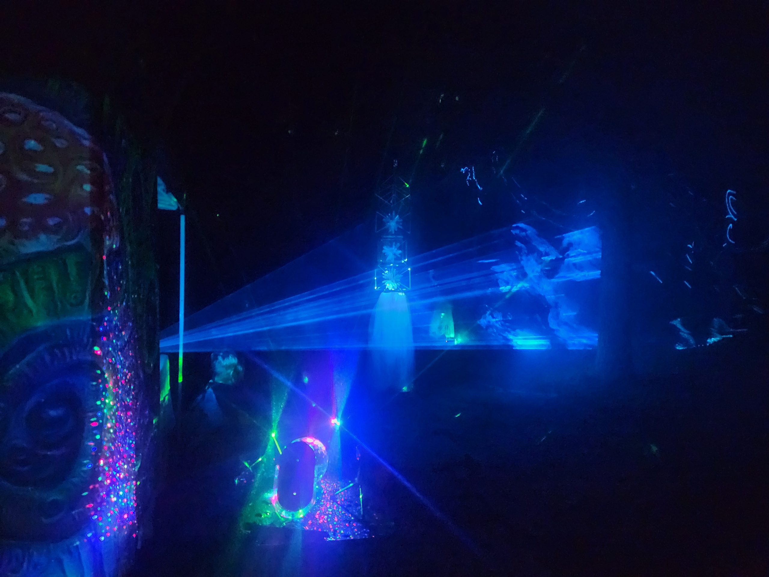 Blue laser beams crossing a festival forest installation