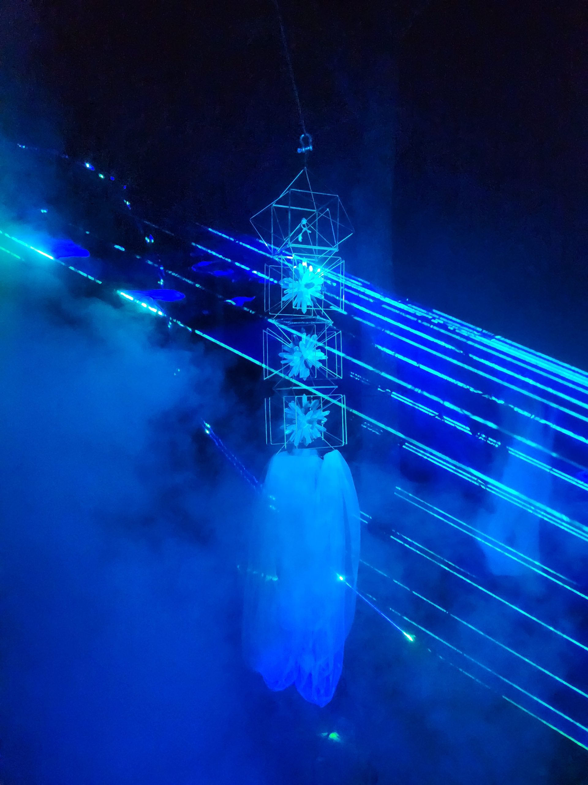 The same lattice tower glowing blue with laser beams and haze after dark